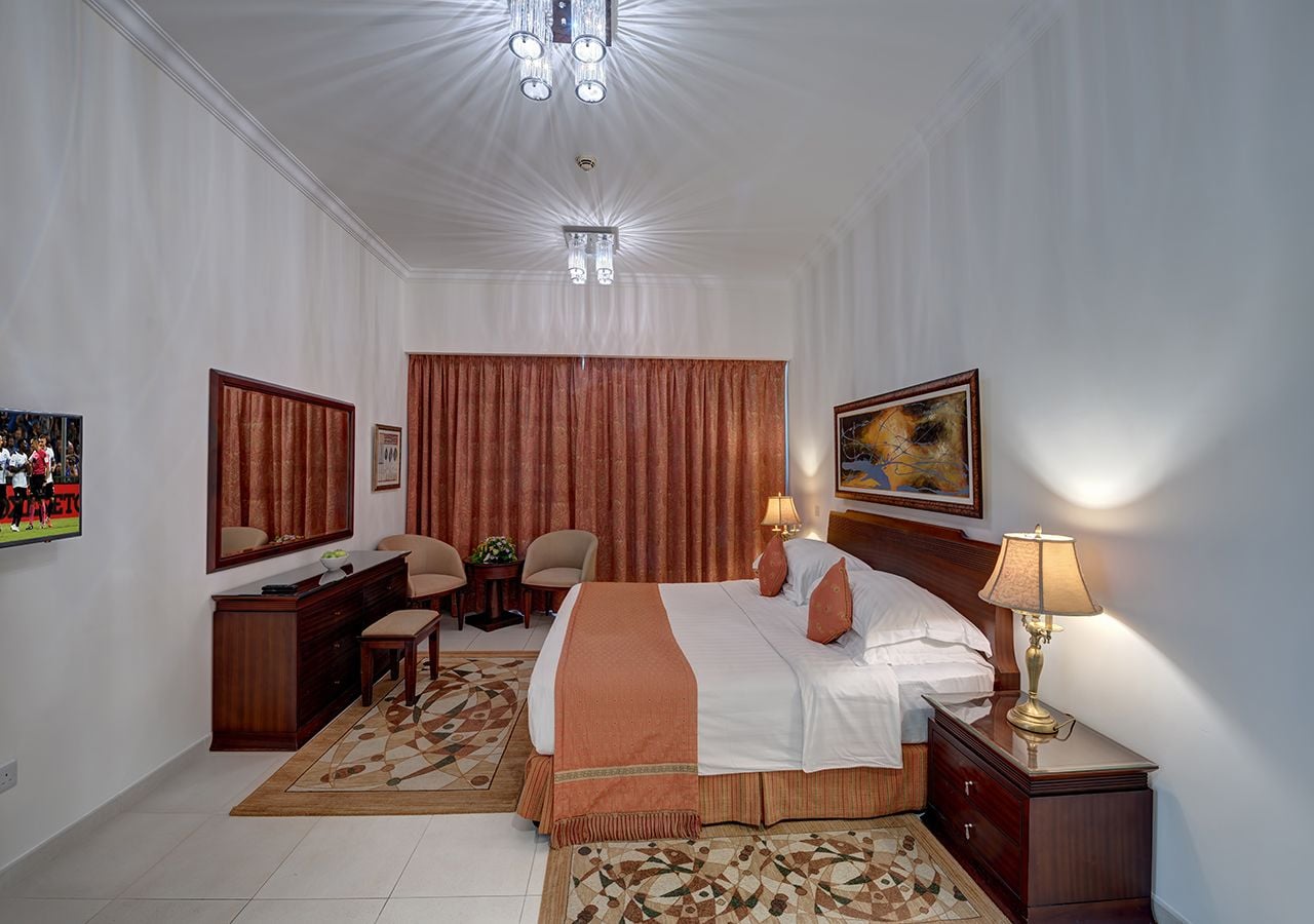 A hotel room with a large bed, a desk, two chairs, a dresser, a nightstand, and a painting on the wall.