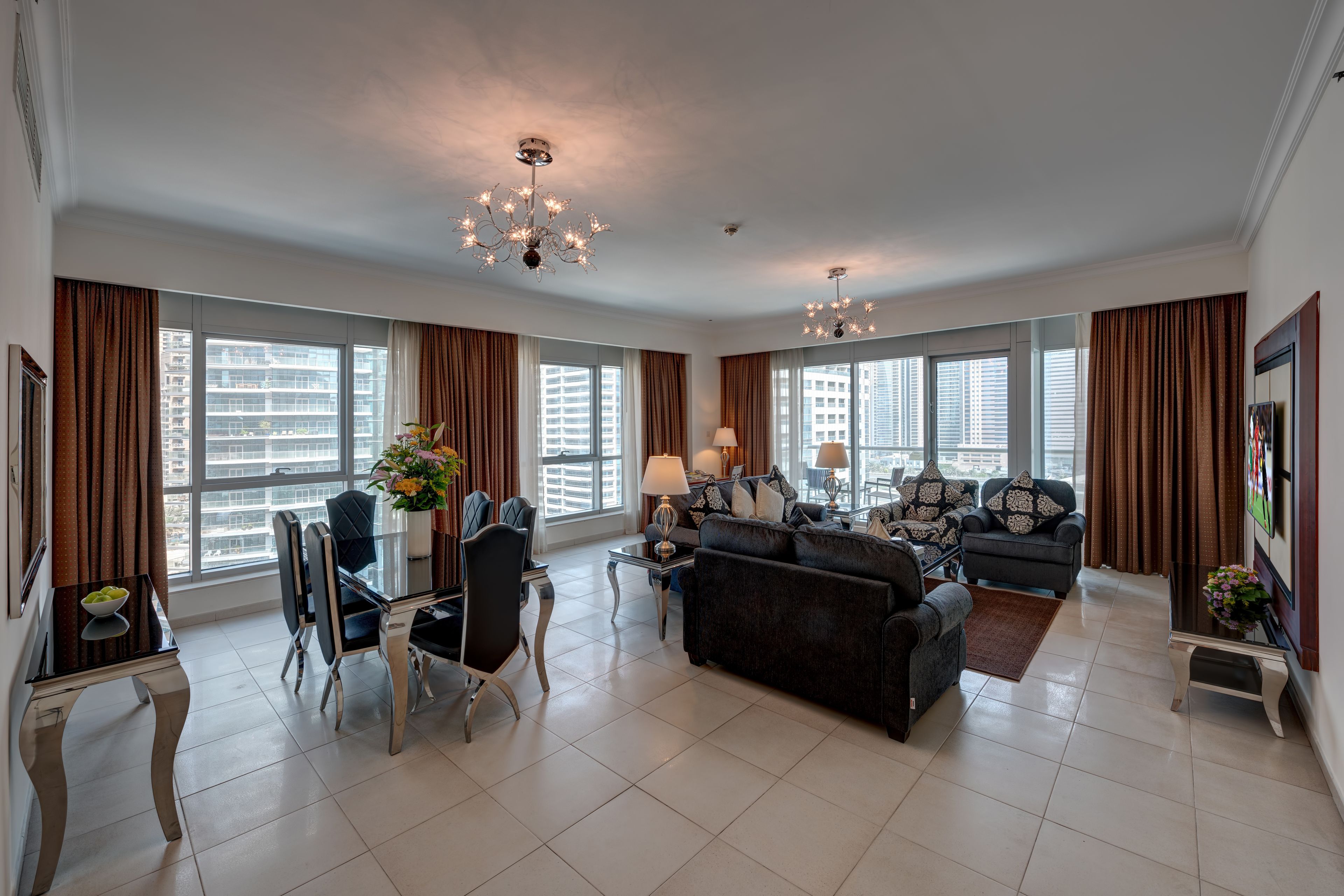 Amplia sala de estar con una lámpara de araña moderna, comedor con mesa de vidrio y grandes ventanales con vistas a la ciudad.