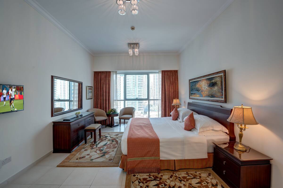 A hotel room with a large bed, a desk with a chair, a television, and a window with curtains.