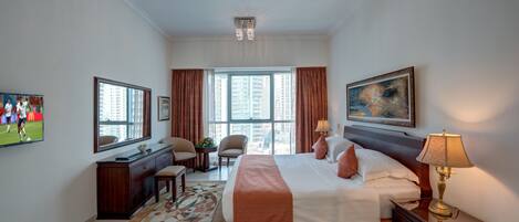 A hotel room with a large bed, a desk with a chair, a television, and a window with curtains.