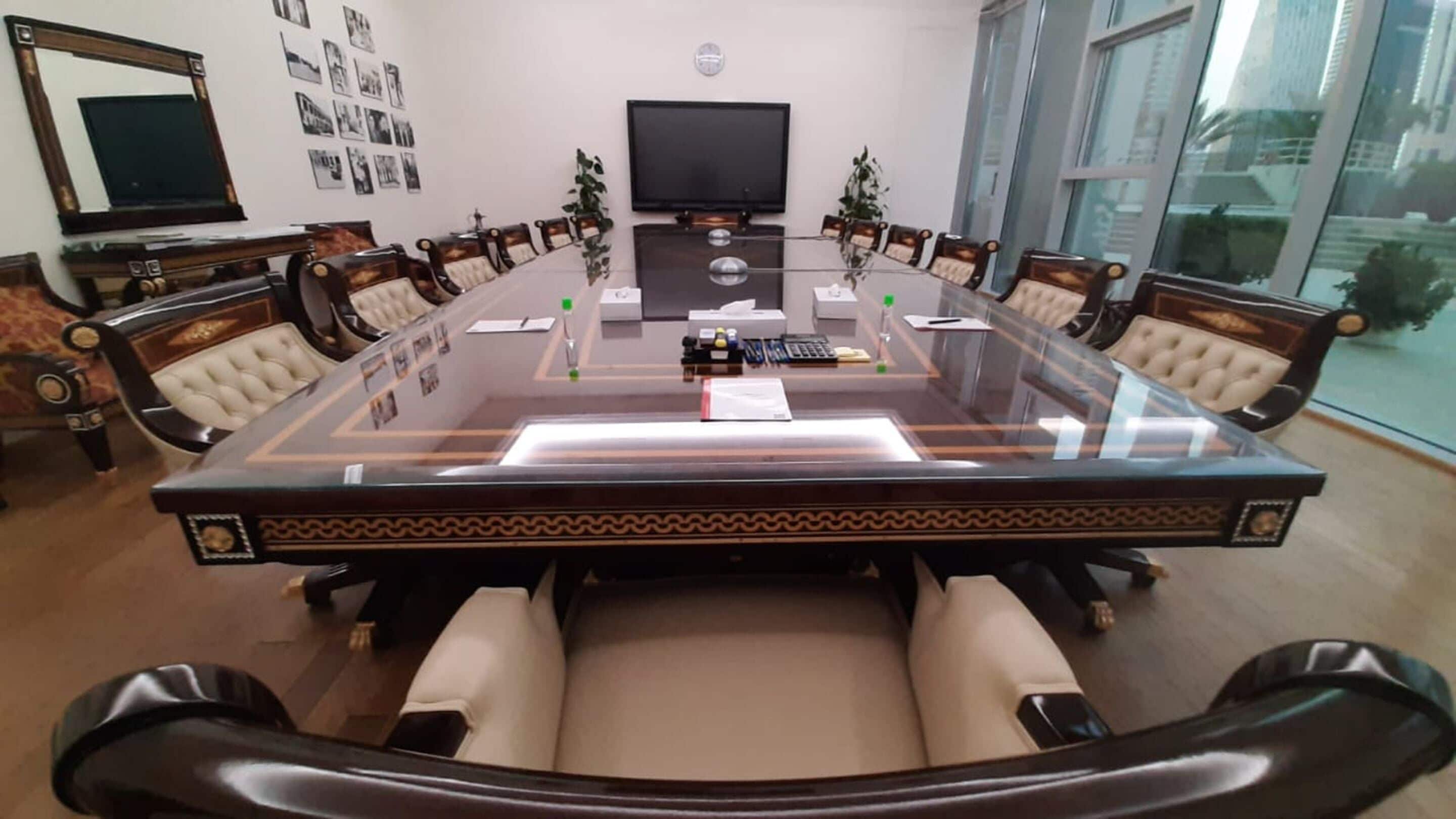 A conference room with a glass table, leather chairs, a television, and framed photos on the wall.