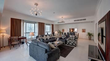 Un salon moderne avec un canapé, des fauteuils, une table basse et un téléviseur. On y trouve des fenêtres avec des rideaux, un lustre et une plante en pot.