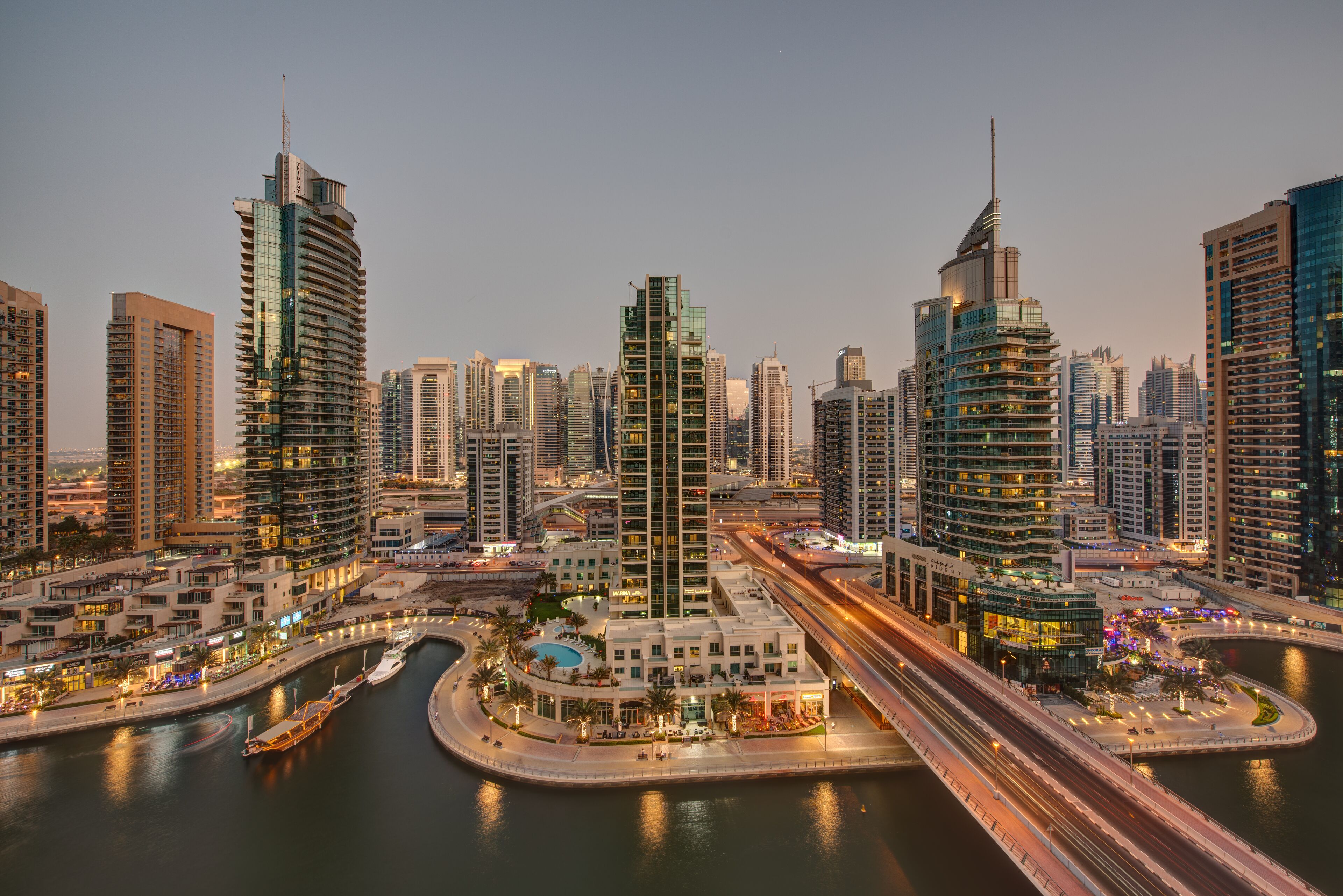 A modern cityscape with high-rise buildings, a marina, and a bridge.