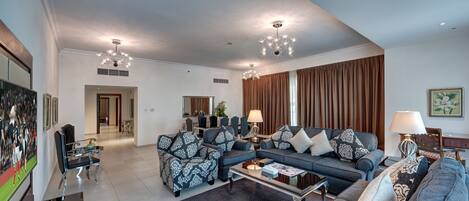 A spacious living room with a sectional sofa, armchairs, and a coffee table. There are two pendant lights and a large window with curtains.