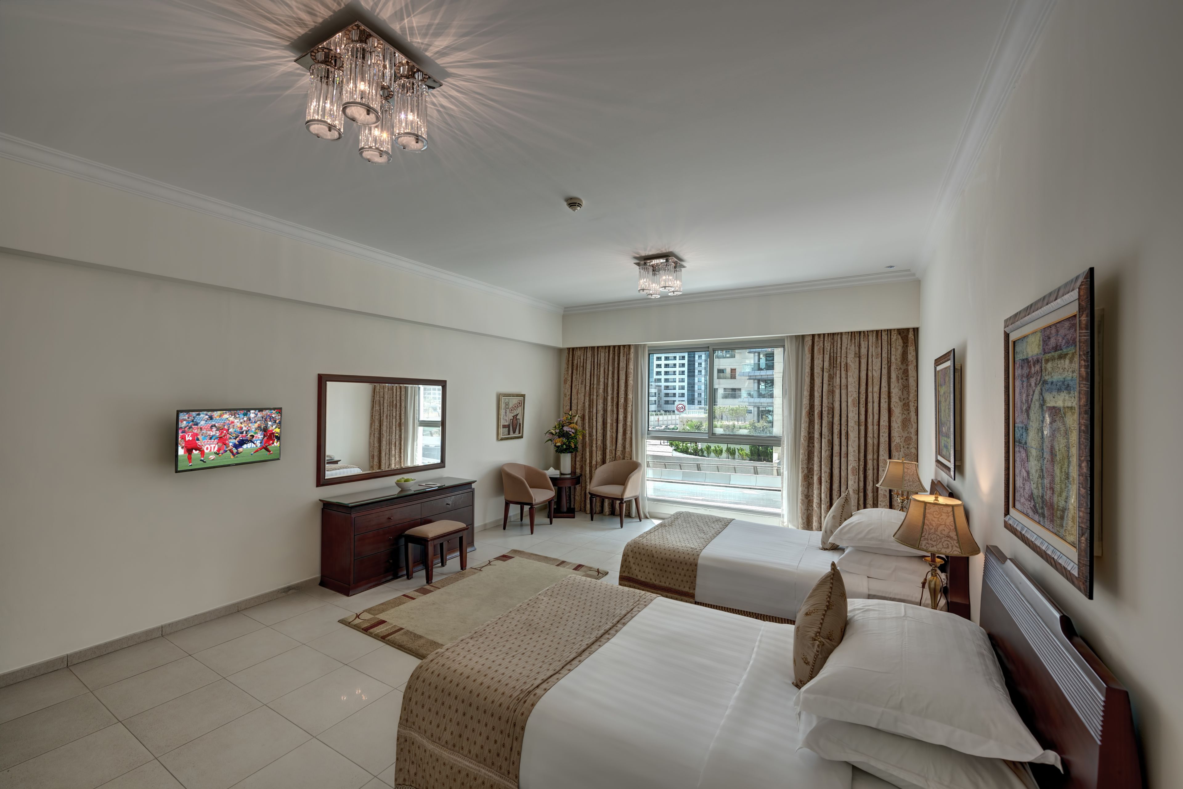A hotel room with two beds, a desk, a chair, a TV, and a large window with curtains.