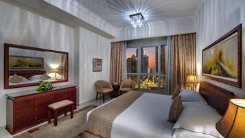 Ein Hotelzimmer mit einem großen Bett, einem Schminktisch, einer Bank, einem Sessel, einem Tisch und Blick auf die Stadt durch das Fenster.