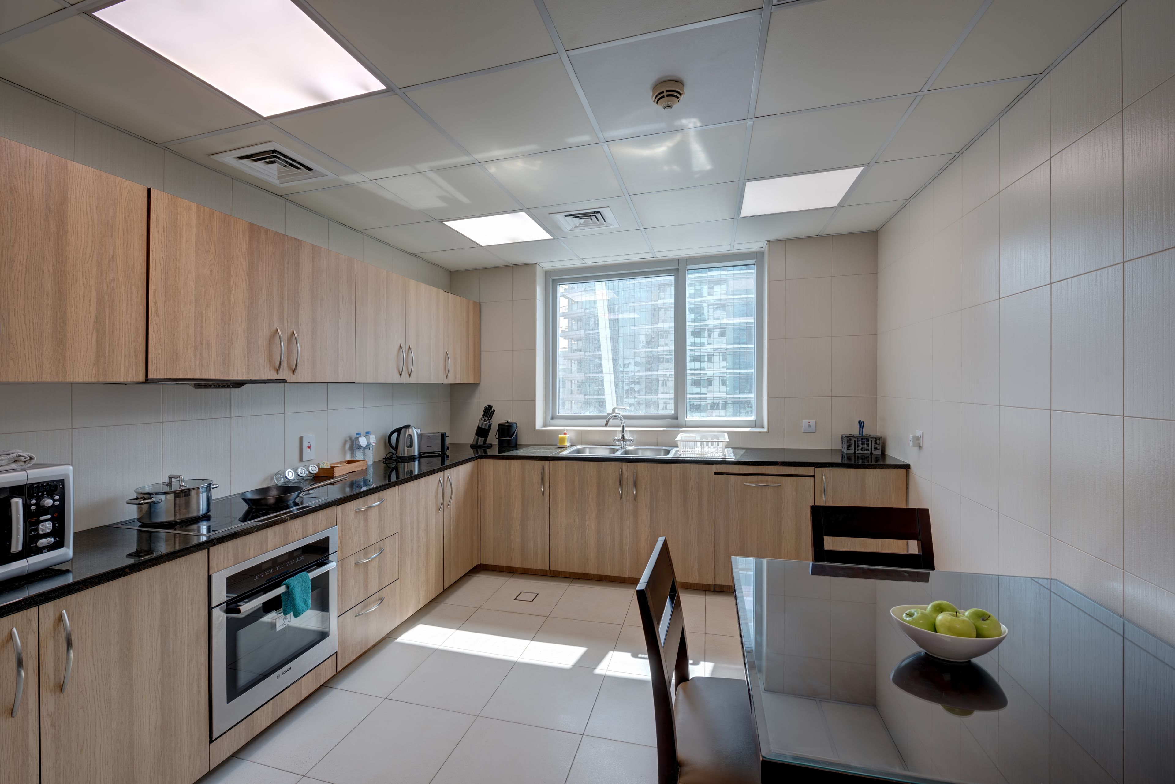 A modern kitchen with wooden cabinets, a built-in oven, a microwave, and a large window providing natural light.