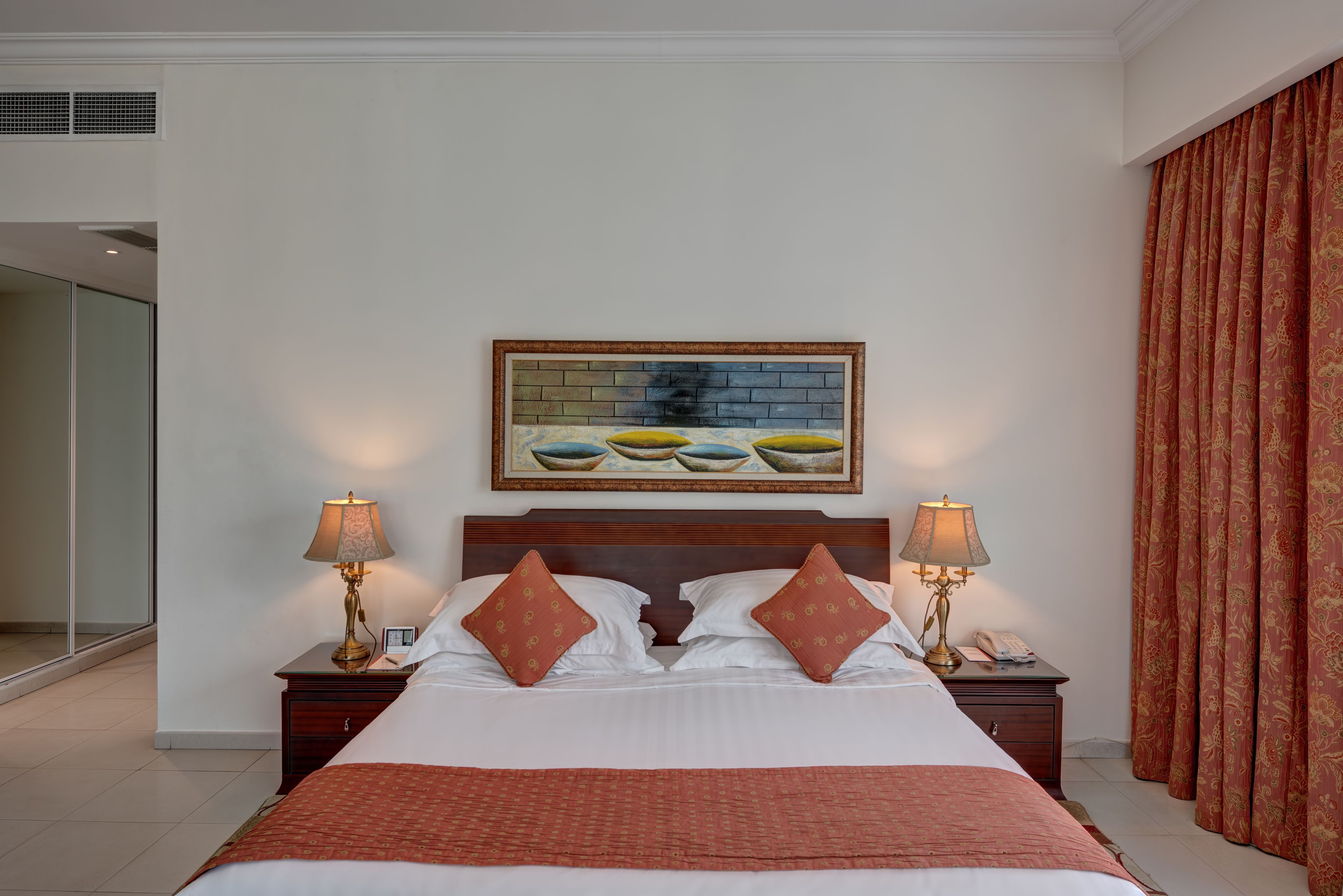 Een hotelkamer met een groot bed, twee nachtkastjes met lampen, een schilderij boven het bed, en een schuifdeur links.