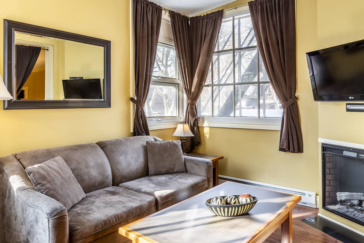 A living room with a sofa, a coffee table with decorative items, a fireplace, and a television mounted on the wall.