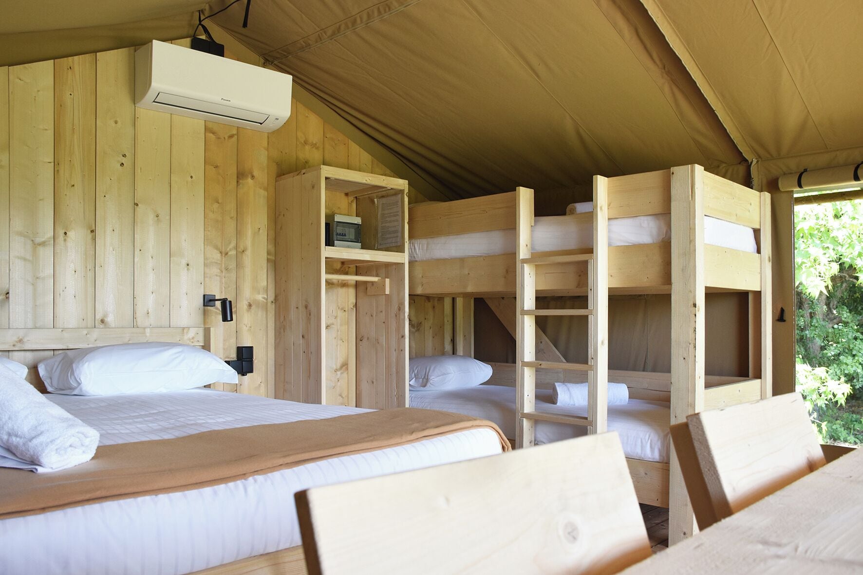 Una cabaña de madera con literas, un ventilador de techo y una ventana con vistas a la vegetación.