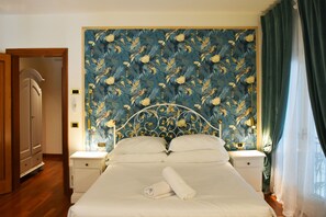 A neatly made bed with white linens and a rolled towel, a nightstand with a lamp, and a wall with a floral pattern.