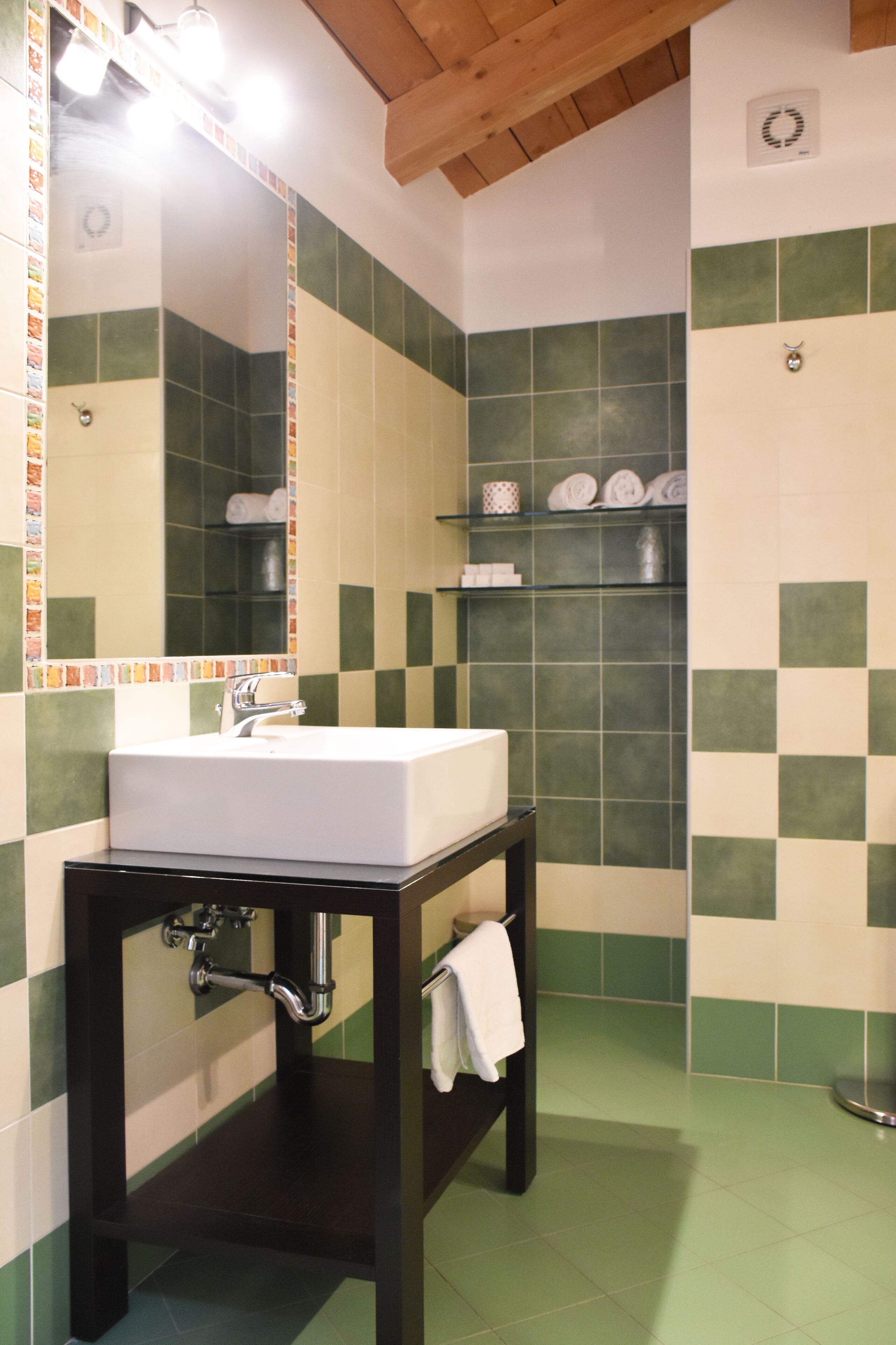 Een badkamer met een witte wasbak, een donker houten wastafelmeubel, groene en witte geruite tegels, een spiegel en een handdoekhouder.