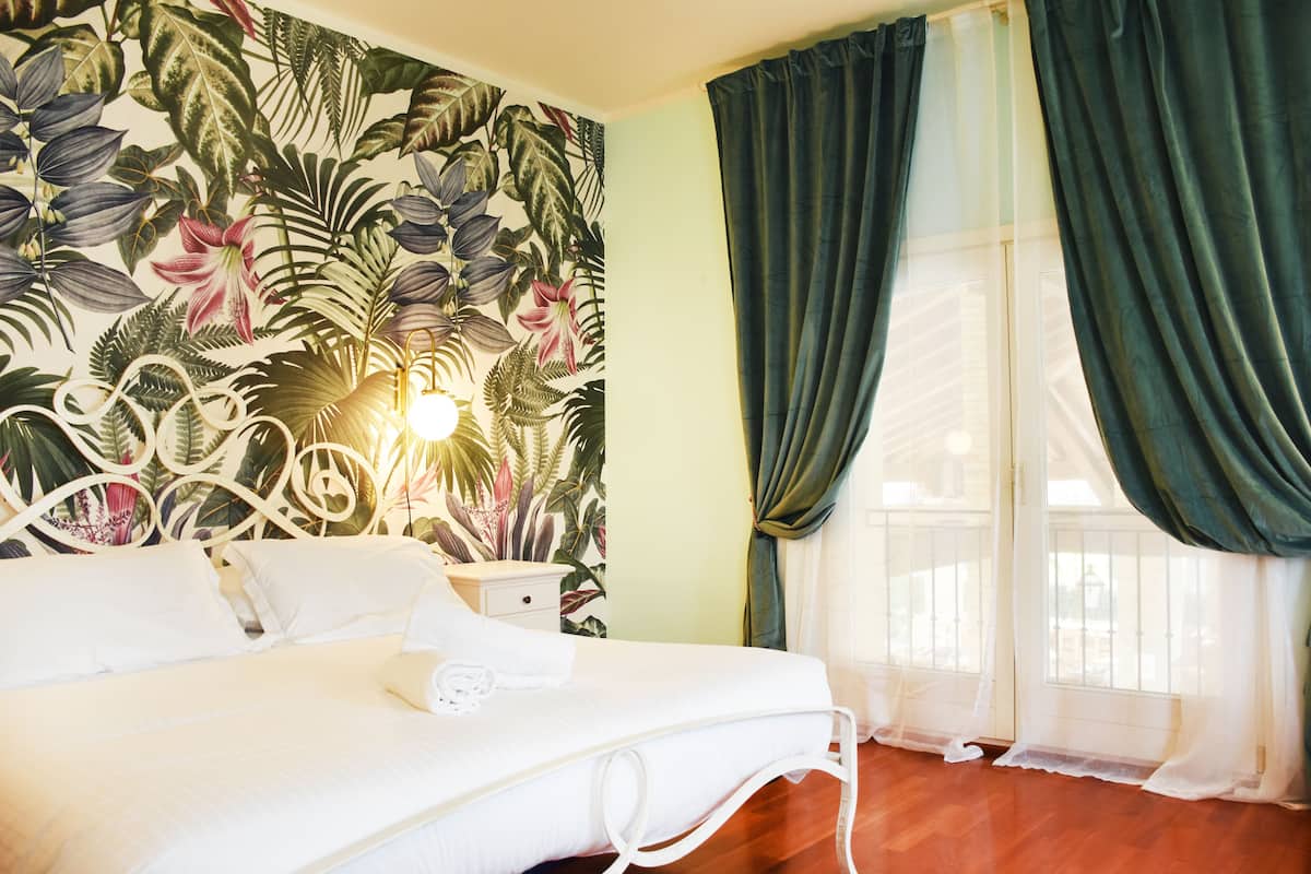 Une chambre d’hôtel avec un lit, une table de chevet, une fresque murale et une fenêtre avec des rideaux.
