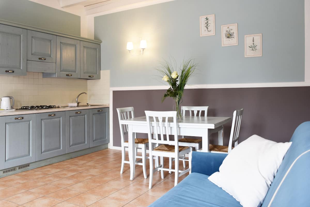 Une cuisine avec des meubles de couleur grise, une table à manger blanche avec des chaises, et un canapé bleu.