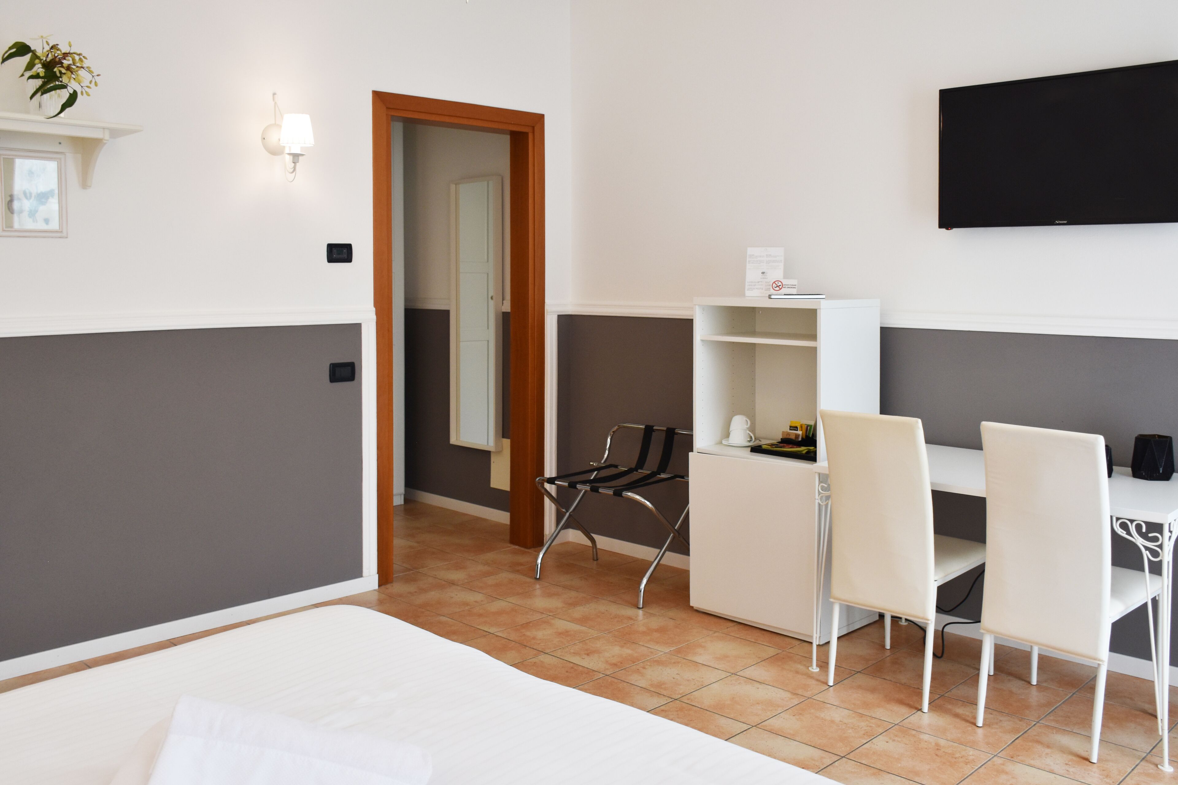 Habitación de hotel con una cama, un escritorio, dos sillas, un televisor y una puerta que da a otra habitación.