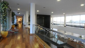 A spacious indoor area with a wooden floor, large windows, and a glass railing overlooking a lower level. - INATEL Vila Ruiva Hotel (Fornos de Algodres)