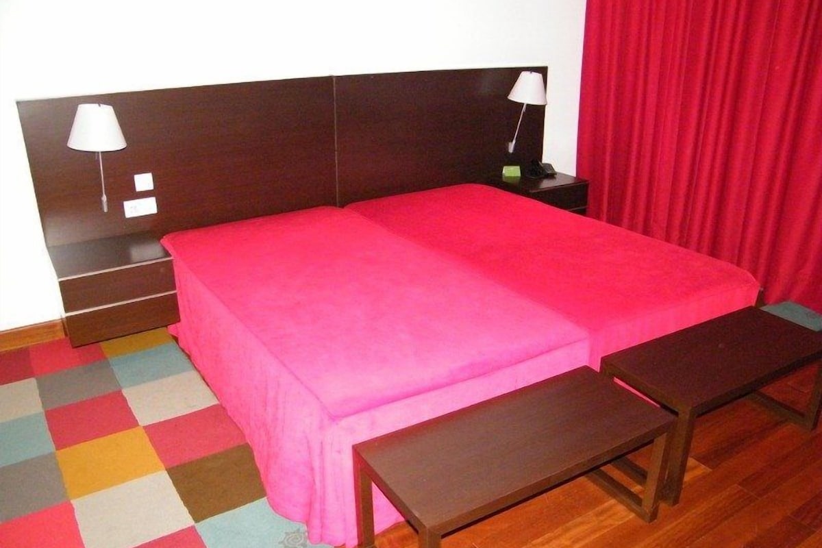 A hotel room with a large bed, two bedside tables, a nightstand, and a colorful checkered floor.