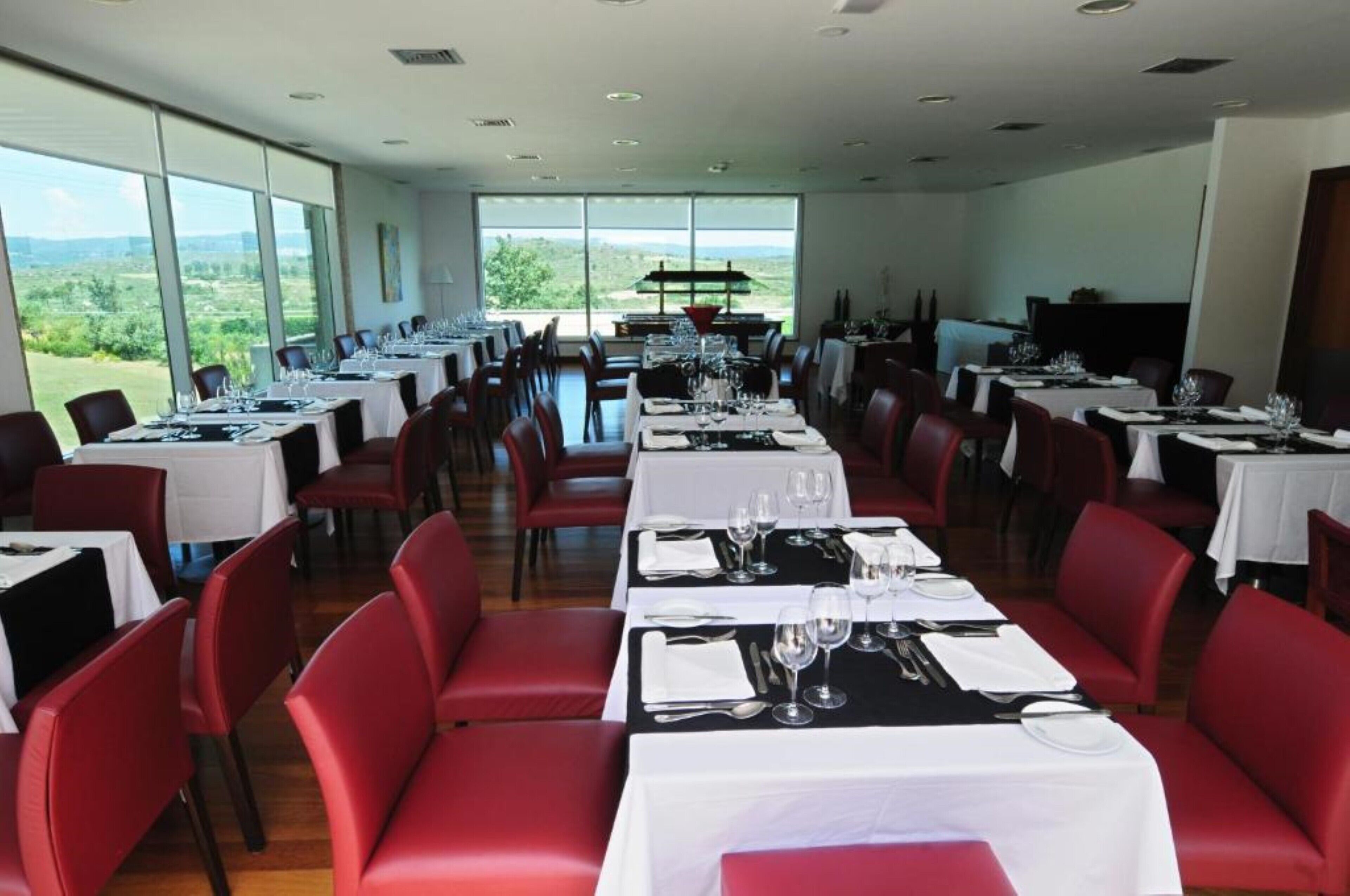Un restaurant doté de nombreuses tables dressées pour le service, de grandes fenêtres offrant une vue sur l’extérieur et d’un décor intérieur moderne.