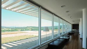 A modern interior with large windows, wooden flooring, and a seating area with a lamp. - INATEL Vila Ruiva Hotel (Fornos de Algodres)