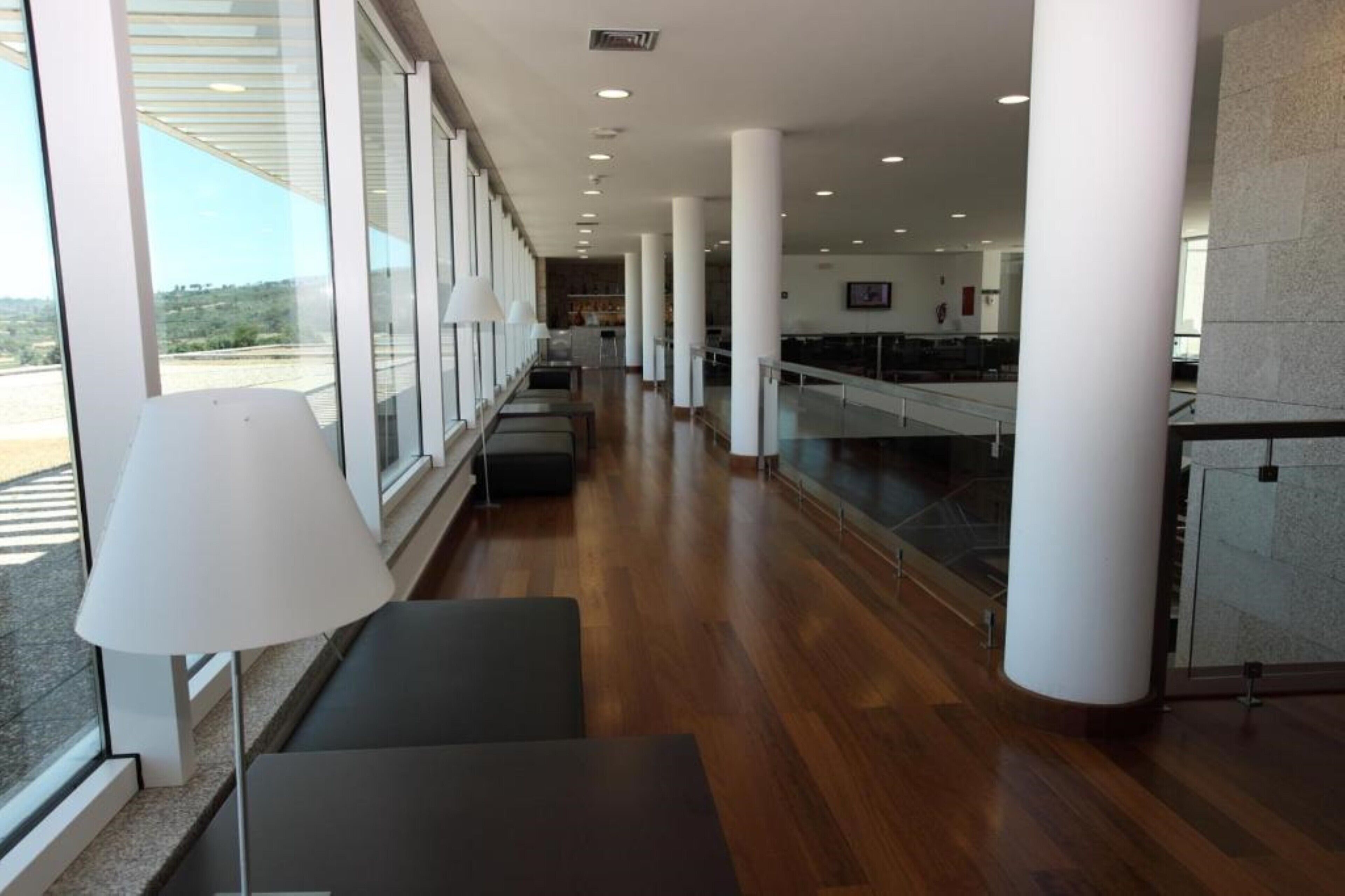 A spacious lobby with wooden flooring, large windows, and a seating area with a lamp.
