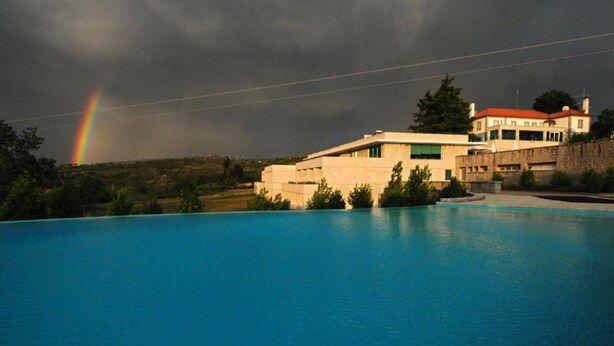 A swimming pool with a view of a building and a rainbow in the background. - INATEL Vila Ruiva Hotel (Fornos de Algodres)