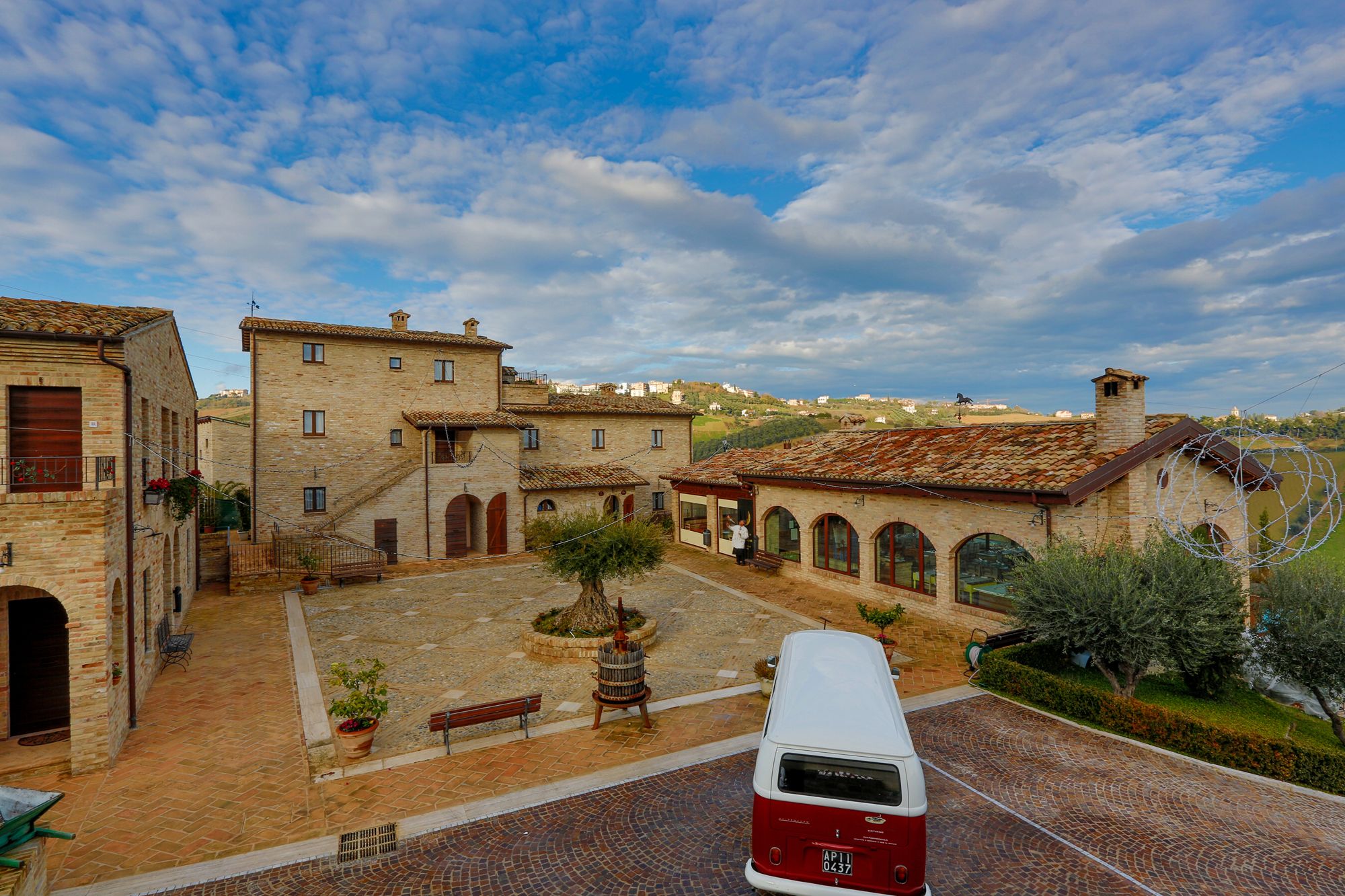 A courtyard with stone buildings, a red and white van, and a clear sky.