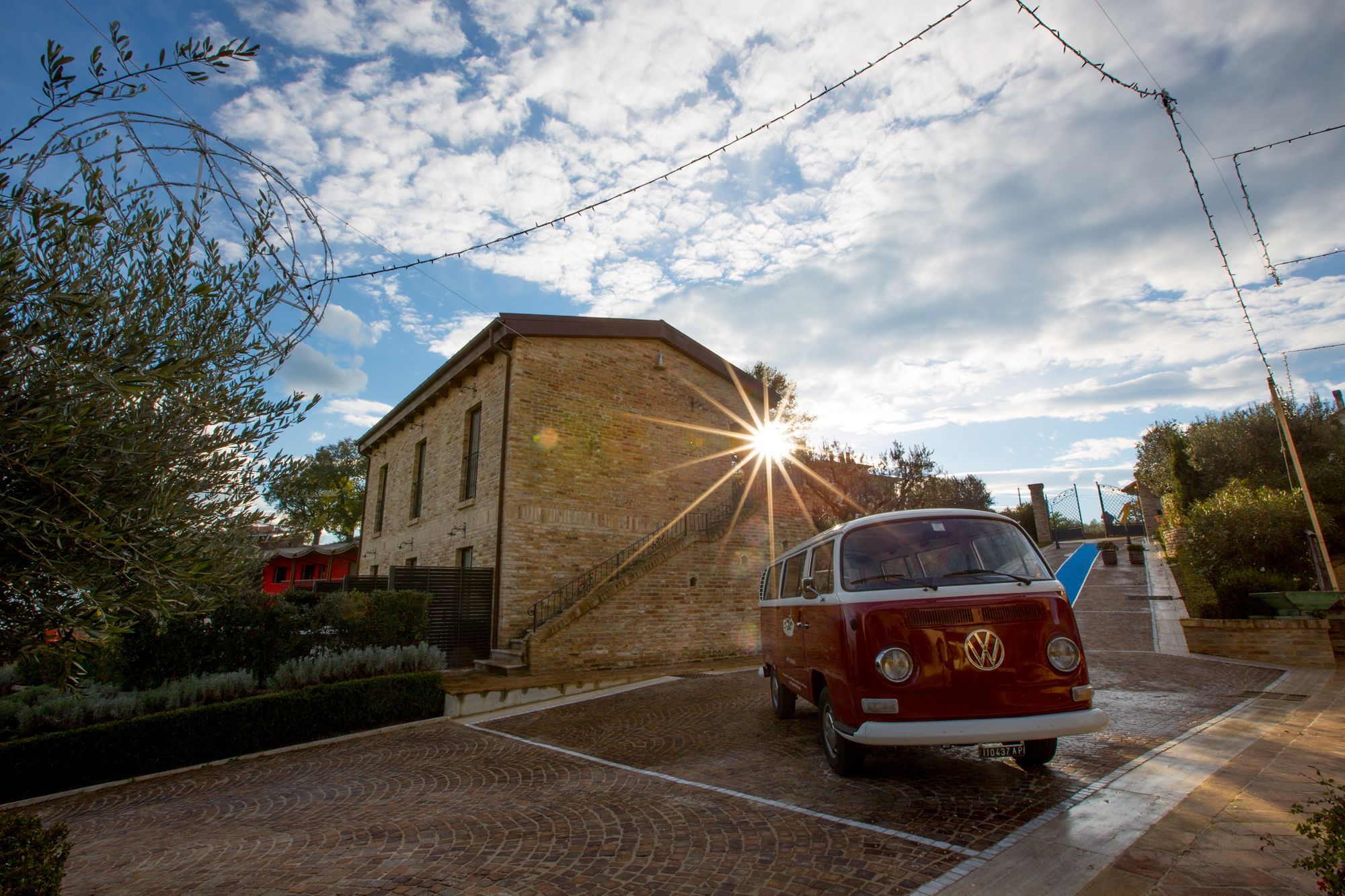 Un vieux combi Volkswagen est garé devant un bâtiment en pierre, avec un chemin pavé de briques qui y mène.