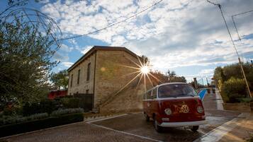 Un vieux combi Volkswagen est garé devant un bâtiment en pierre, avec un chemin pavé de briques qui y mène.