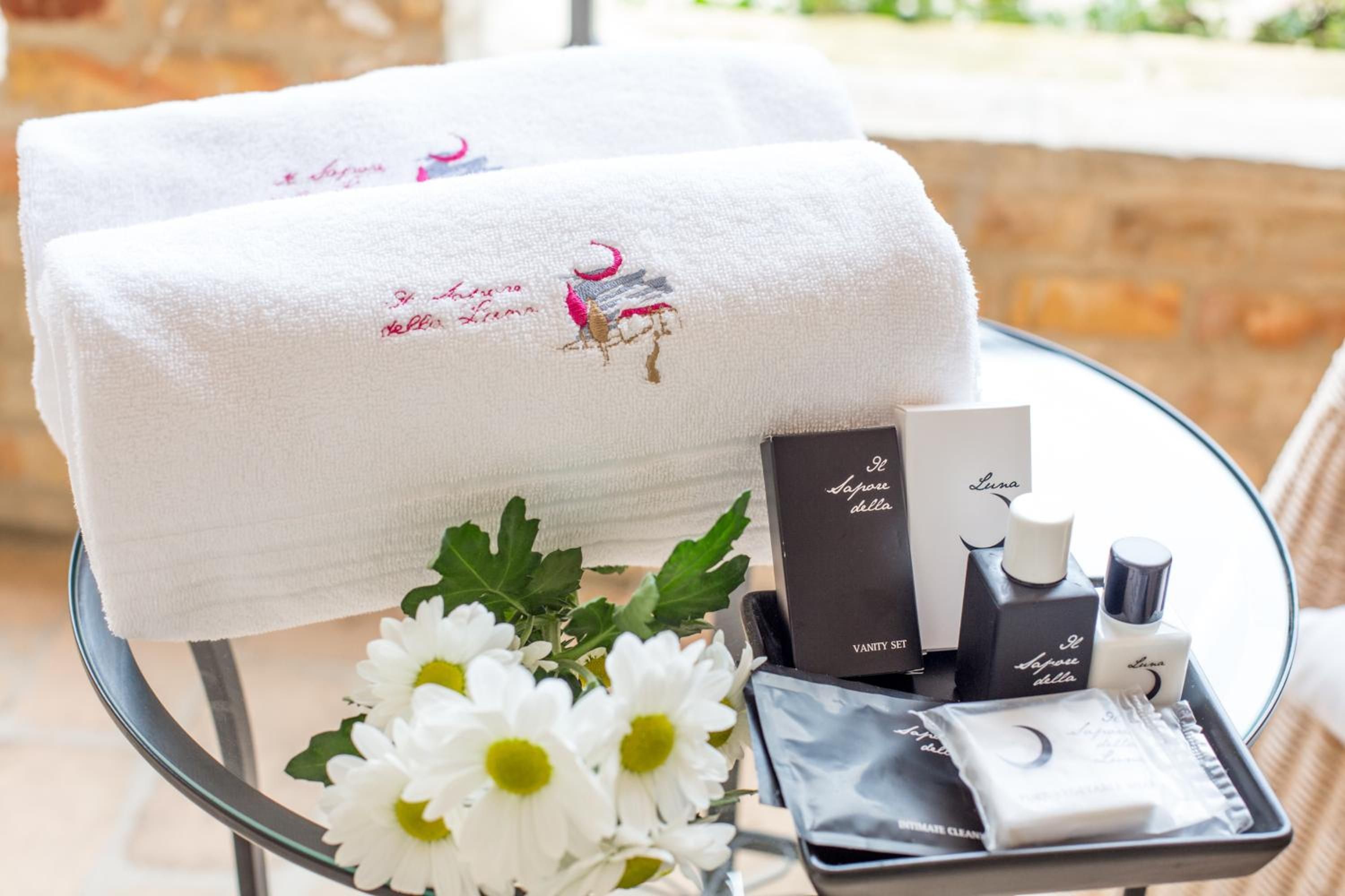 A glass table with a towel, toiletries, and a flower arrangement.