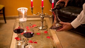 Une personne verse du vin dans des verres sur une table décorée de bougies et de pétales de rose.
