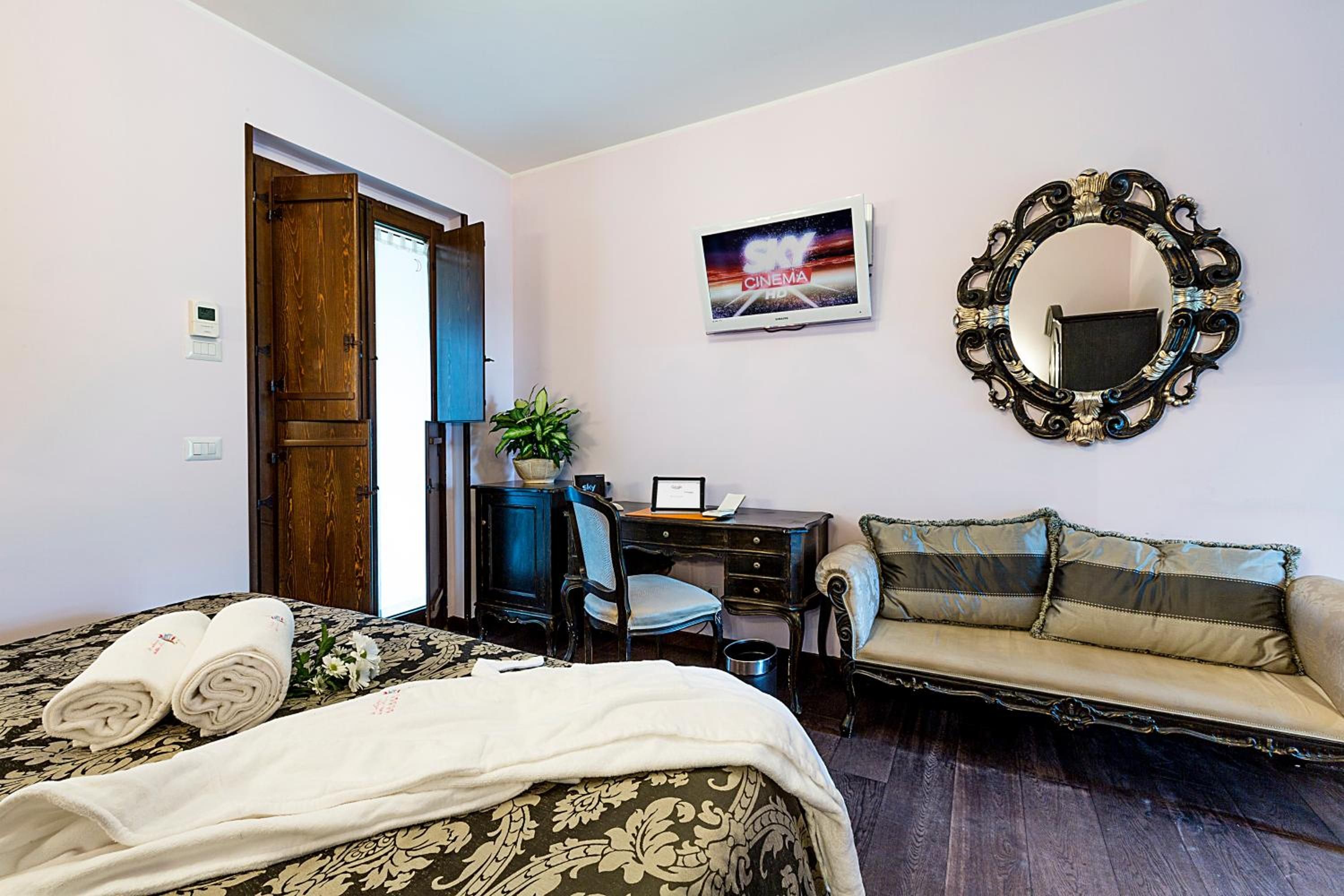 Un dormitorio con cama, escritorio, sillón, sofá, espejo y televisor de pared.