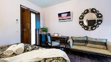 Un dormitorio con cama, escritorio, sillón, sofá, espejo y televisor de pared.