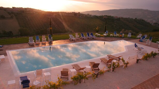 Une piscine entourée d’une terrasse, agrémentée de chaises longues et de tables, et offrant une vue sur les collines.