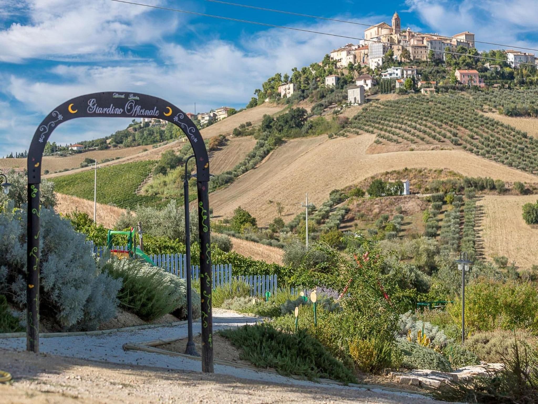 Un paysage rural avec un vignoble, un village perché sur une colline et un panneau indiquant une région viticole.