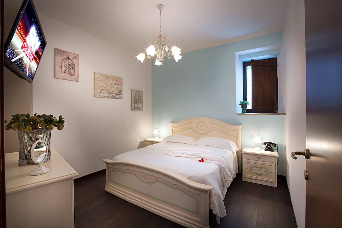 Un dormitorio con cama, mesitas de noche, televisor y obras de arte en las paredes.
