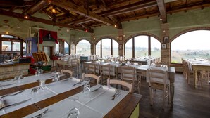 Un restaurant avec des poutres en bois, des fenêtres en arc de cercle et des tables dressées pour le dîner.