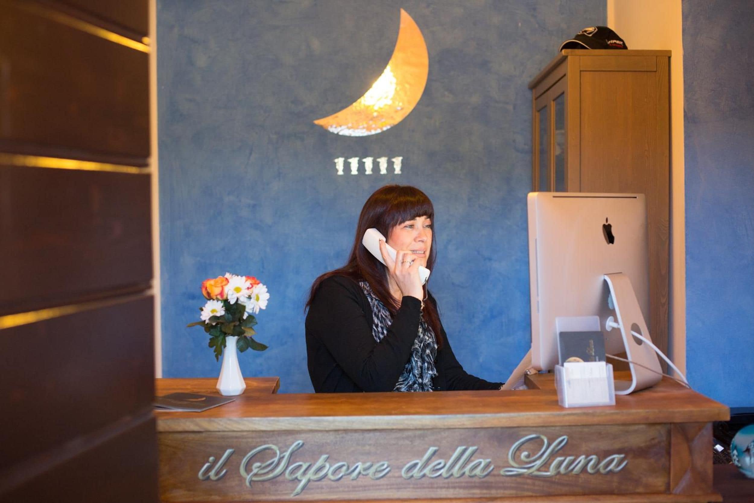 A reception desk with a wooden counter, a computer, and a vase with flowers. The wall behind has a crescent moon design and the number '11111'.