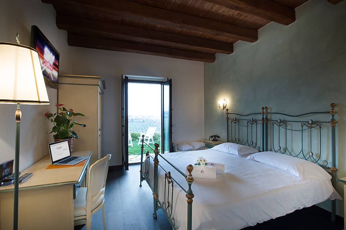 Habitación de hotel con cama, escritorio con laptop, silla, lámpara y vista al exterior.