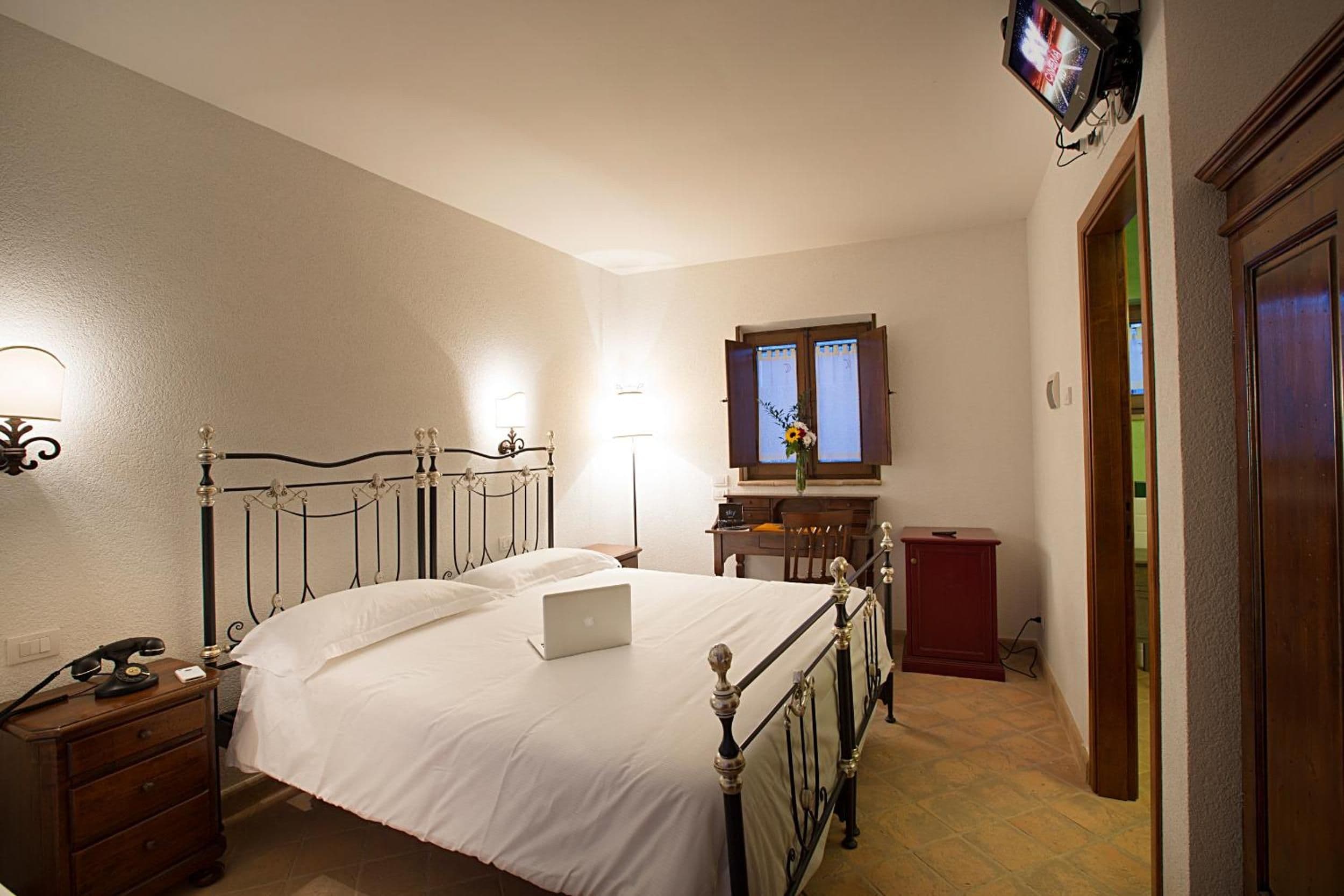 A bedroom with a bed, a desk, a chair, a lamp, a television, and a door.