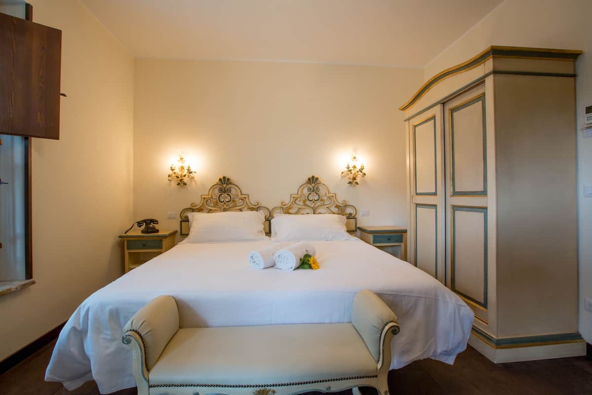 Una cama bien hecha con un banco, dos mesitas de noche y un armario en una habitación de hotel.