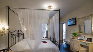 Une chambre à coucher avec un lit à baldaquin, un bureau avec un ordinateur, une chaise, une télévision et un grand miroir.