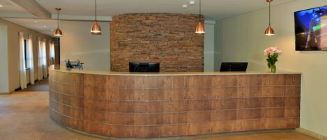 A reception desk with a stone wall backdrop, pendant lighting, and a flat-screen TV on the wall.