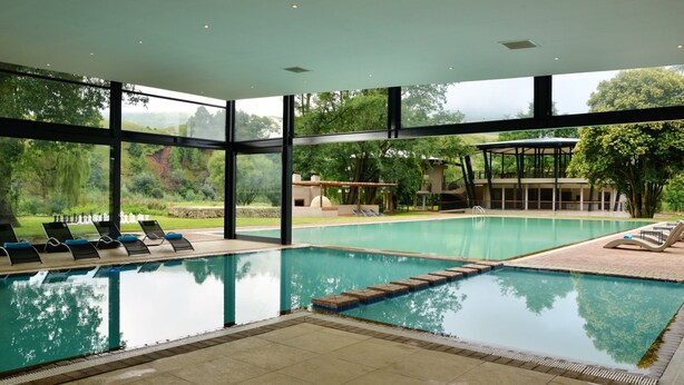 A swimming pool with clear water, surrounded by lounge chairs and a covered seating area. - Premier Resort Sani Pass (Himeville)