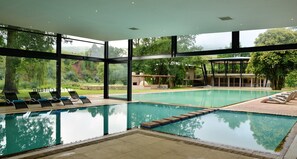 A swimming pool with clear water, surrounded by lounge chairs and a covered seating area. - Premier Resort Sani Pass (Himeville)