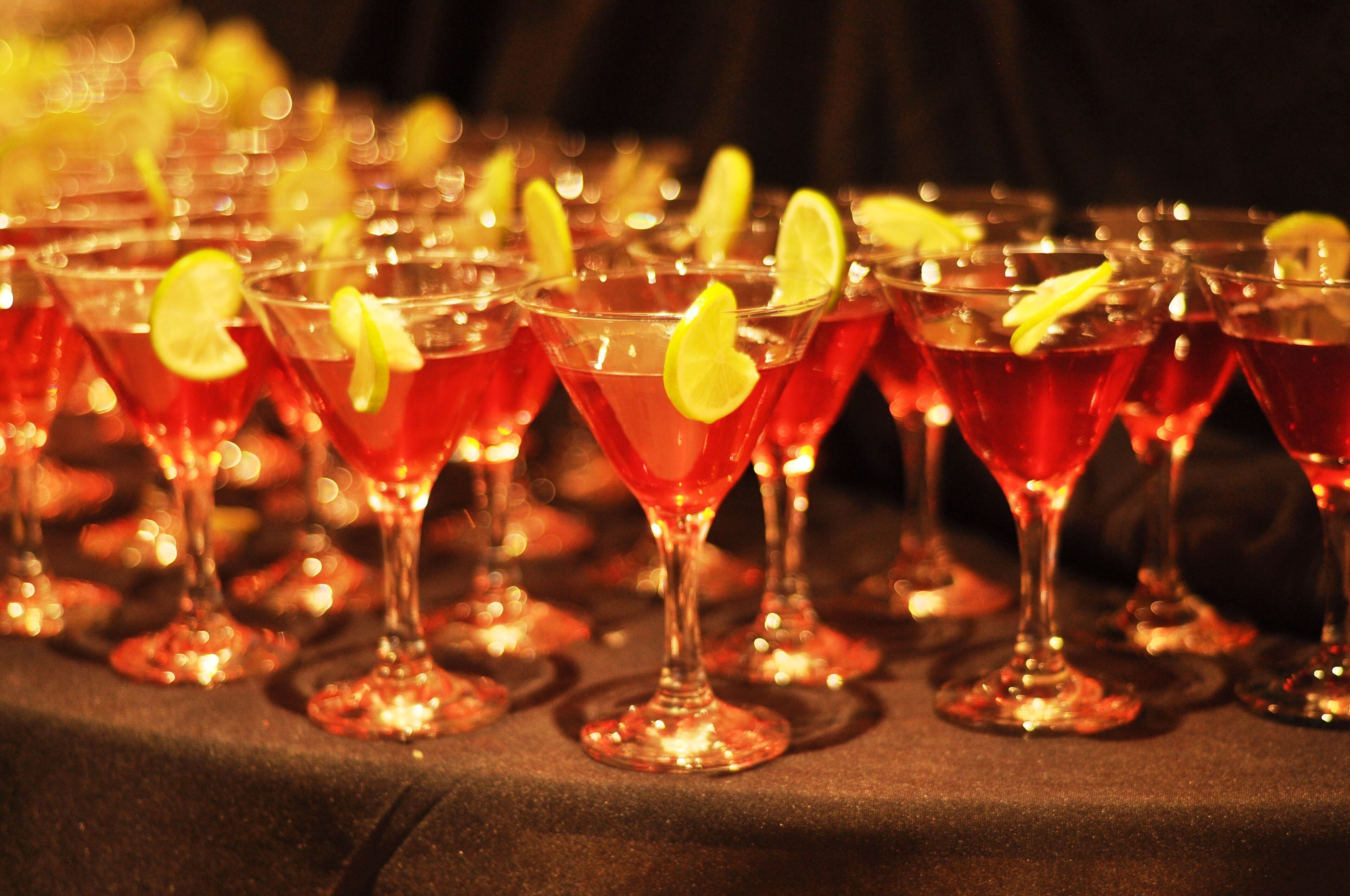 A row of martini glasses filled with a red beverage, garnished with lemon slices, on a table.