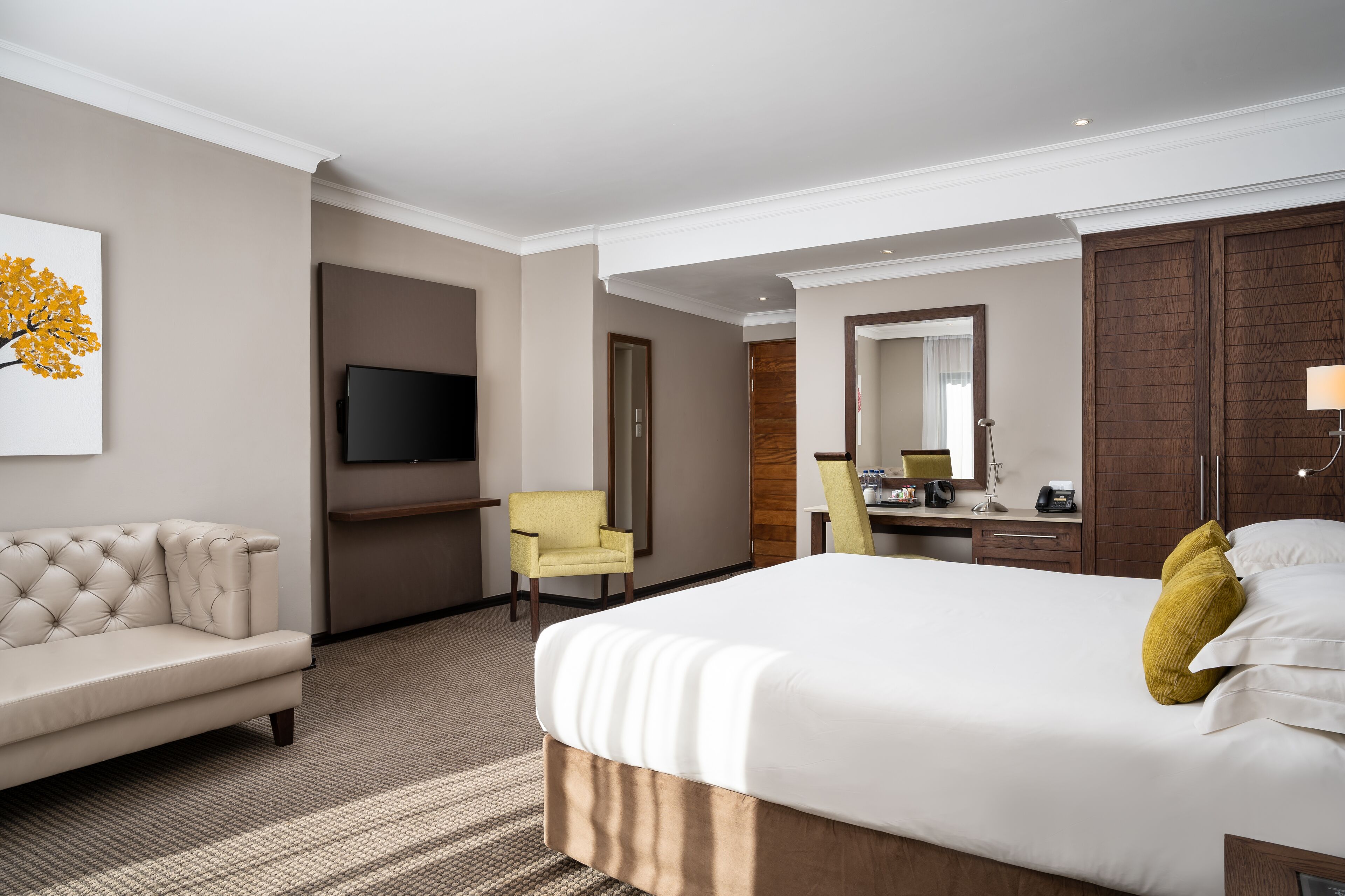 A hotel room with a large bed, a sofa, a desk, a chair, a television, and a mirror.