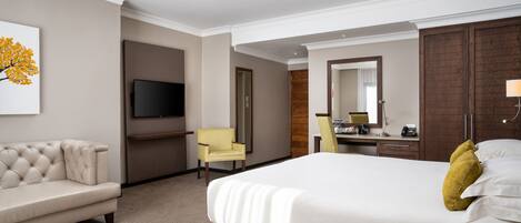 A hotel room with a large bed, a sofa, a desk, a chair, a television, and a mirror.