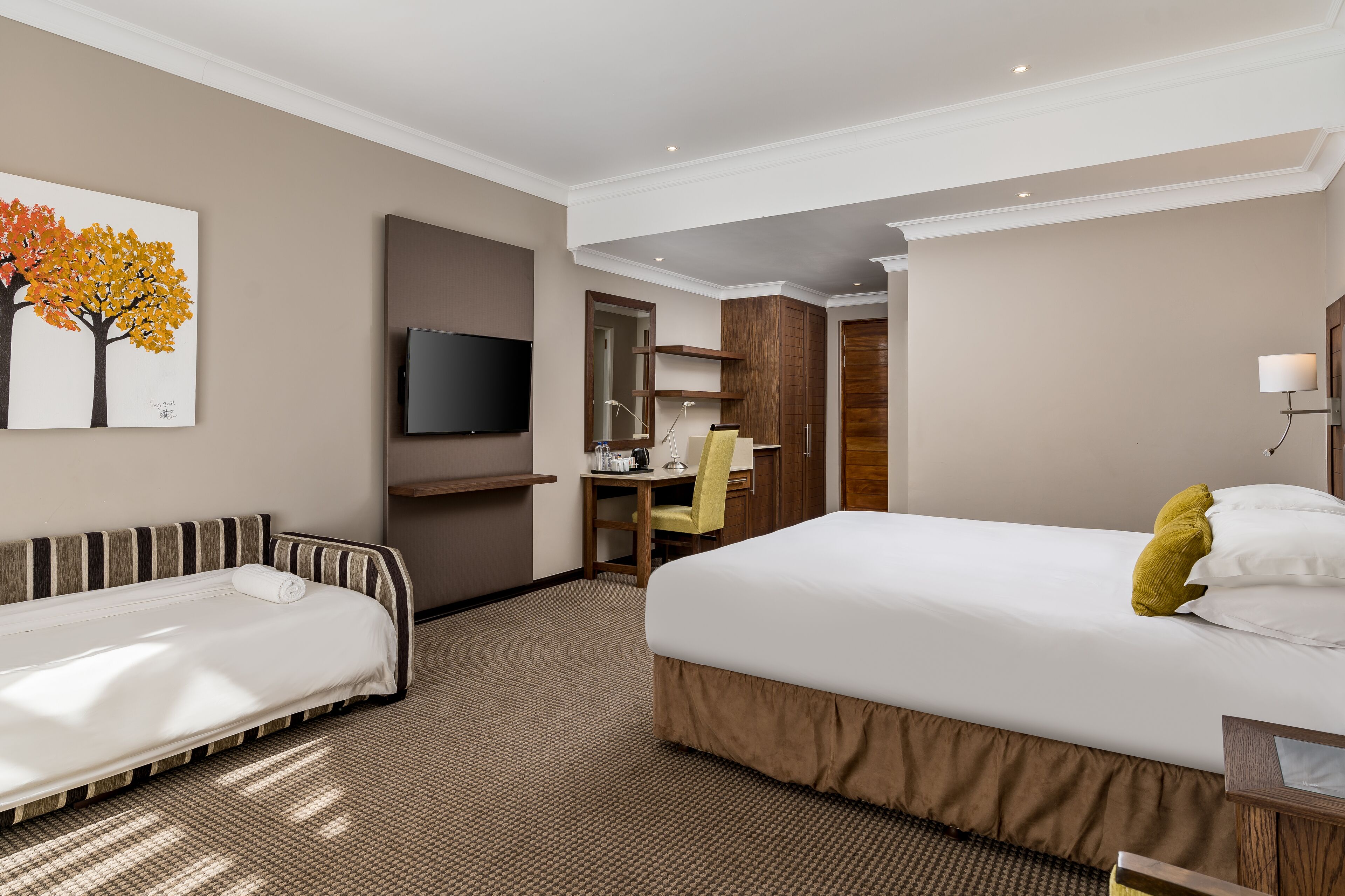 A hotel room with a bed, a desk, a chair, a TV, and a painting on the wall.
