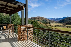 A balcony with a stone wall, metal railing, and a view of a valley with mountains in the background. - Premier Resort Sani Pass (Himeville)