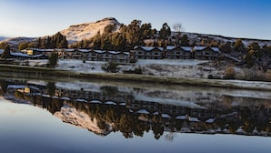 A hotel with multiple buildings reflecting on a calm body of water, surrounded by snow-covered hills and trees. - Premier Resort Sani Pass (Himeville)